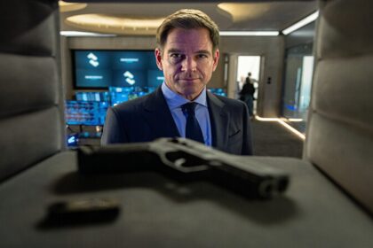 Michael Weatherly as Tony DiNozzo in a suit, looking directly forward with a serious expression, with a handgun in the foreground, from NCIS: Tony & Ziva Season 1 Episode 1 - No Country is Safe
