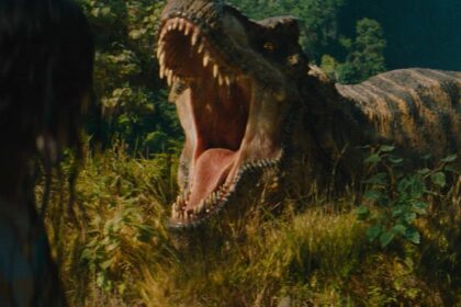 A massive T-Rex roars, jaws wide, at a person with their back to the camera, amidst lush green foliage in a scene from Jurassic World Rebirth.