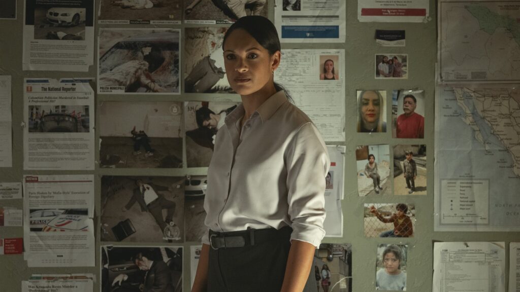 Movie still from The Accountant 2 - Marybeth Medina (Cynthia Addai-Robinson) stands in front of a wall covered with various crime scene photos, notes, and a map, looking contemplative.